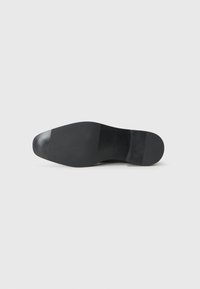 Zool van een zwarte schoen weergegeven op een witte achtergrond, die een glad, vlak oppervlak en minimale merkdetails laat zien.