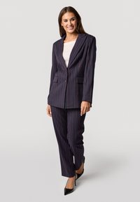 Completo a righe navy, con giacca doppiopetto dotata di due tasche frontali e pantaloni affusolati coordinati. Indossato con tacchi neri.