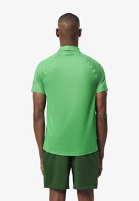 Camisa polo verde de manga corta, fabricada con un material suave y ligero. Presenta un logotipo sutil en la nuca. Combinada con pantalones cortos verde oscuro.