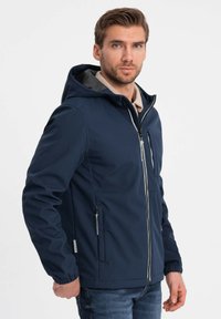 Mørkeblå jakke med hætte, lynlås, elastiske manchetter og sidelommer. Har en gråforet hætte og et strømlinet design.