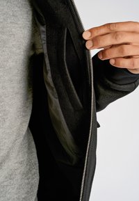 Svart jacka med slät utsida och mjukt innerfoder. Dragkedja och synlig handficka. Grå tröja under.