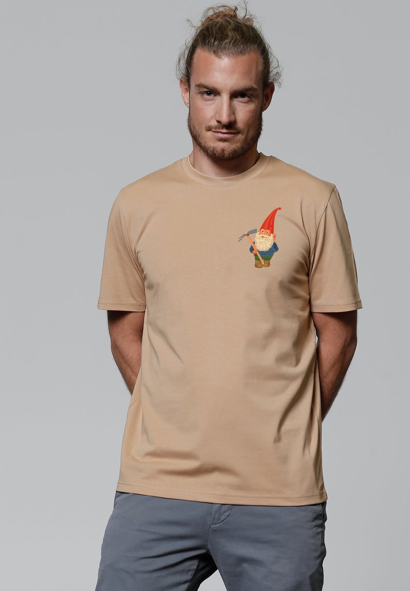 Beige katoenen t-shirt met een kleurrijke gnomenafbeelding op de borst. Korte mouwen en een ronde hals. Soepele textuur.