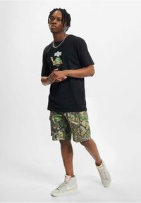 Sort bomulds t-shirt med et grafisk print, parret med camouflage cargo shorts. Fodtøj: lys grå høj-tops sneakers.