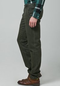 Proste spodnie w ciemnozielonym kolorze wykonane z mieszanki bawełny, charakteryzujące się gładką fakturą i bocznymi kieszeniami, zestawione z brązowymi sznurowanymi butami.