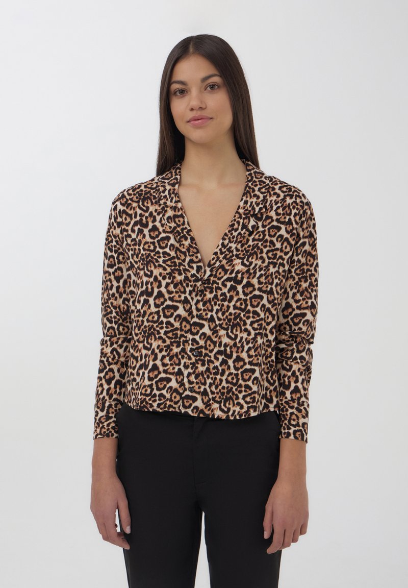 Blusa a stampa leopardata con maniche lunghe, colletto e chiusura a bottoni. Realizzata in tessuto morbido nei colori beige, marrone e nero. Vestibilità aderente.
