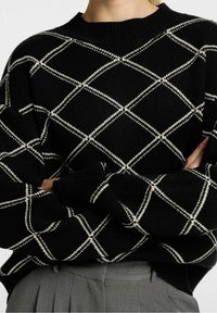 Svart stickad tröja med ett vitt diamantsmönster, ribbat rundhals, och oversize passform; strukturerad tyg med rullade ärmslut.