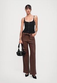 Top senza maniche nero con zip e lacci laterali; pantaloni in pelle marroni a gamba larga; borsa nera con borchie; scarpe nere a punta.