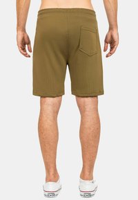 Shorts marroni, lunghi fino al ginocchio, con un tessuto texturizzato, cintura elastica e tasca posteriore; indossati con sneaker bianche.