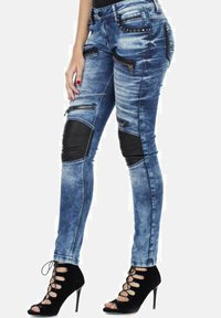 Verbleekte blauwe skinny jeans met zwarte leren accenten op de knieën, ritsen op de zakken en studs aan de taille. Draag met zwarte hakken.