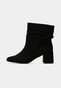 Μαύρο σουέντ μποτάκι μεσαίου μήκους μέχρι τη μέση της γάμπας, με χαλαρή επάνω γραμμή και τακούνι τύπου block, σε απλό λευκό φόντο.