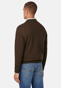 Pruun fliiskardigan, millel on ümmargune krae, soonikkoes varrukad ja alumine äär, koos helesiniste teksadega, millel on kaks tagumist taskut.