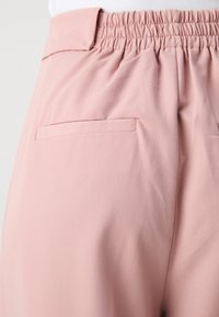 Rosa bukser med elastisk talje, med en glat, mat tekstur og en diskret baglomme detalje.