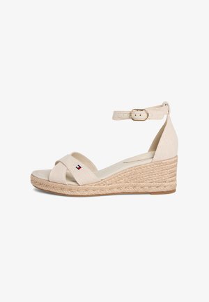 Beige wedge sandal with woven heel, ankle strap buckle, and crossed front straps featuring a small flag logo.