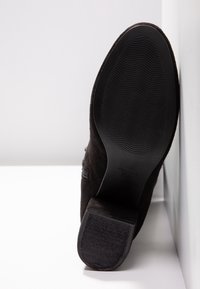 Černá kotníková bota z broušené kůže s texturovanou podrážkou, zaoblenou špičkou a nízkým stohovaným podpatkem. Viditelný boční šev.