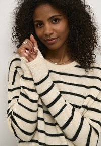 Maglione lavorato a maglia color crema con righe orizzontali nere. Tessuto morbido, polsini a coste e scollo ampio. Design semplice e vestibilità rilassata.