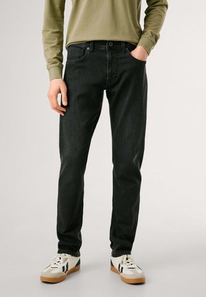 Jeans de mezclilla negra con un corte recto, que cuentan con cinco bolsillos, ligeras marcas de desgaste y una cintura de altura media, combinados con zapatillas blancas.