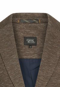 Struktureret brun blazer med marineblå foring, der har en bred revers og mærket "Camel Active" indeni. Størrelse 50 angivet på mærket.