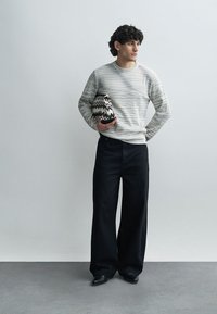 Ljusgrå randig stickad tröja, svarta vida byxor, håller en svartvit väska med zickzackmönster. Minimalistisk design, slät textur.