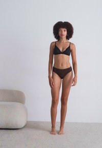 Black lace bralette with triangular cups and thin straps paired with brown striped high-waisted bikini briefs. Smooth, minimal design.