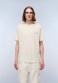 Beige bomulds t-shirt med korte ærmer og rund halsudskæring. Har et lille, tonalt logo på venstre bryst. Glat tekstur.