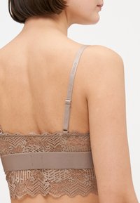 Spetsbralette i en mjuk beige nyans. Har intrikata spetstillämpningar, justerbara axelband och ett slätt band för stöd.