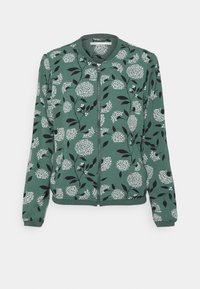 Grön zip-jacka med ett blommigt mönster i vitt och svart, med ribbad krage och manschetter, tillverkad av ett mjukt, texturerat tyg.