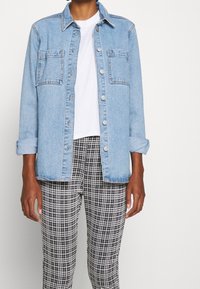 Ljusblå denimjacka med två framfickor och knäppt stängning, bärs över en vit t-shirt och svart-vitrutiga byxor.