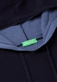 Navyblauwe hoodie met een lichtblauwe binnenvoering, voorzien van een groene "United Colors of Benetton" label bij de hals.