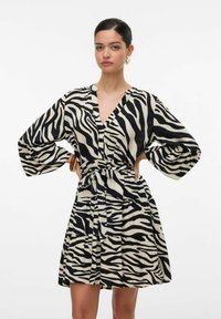 Vestido con estampado de cebra en negro y crema. Presenta un escote en V, mangas anchas, cintura ceñida con un lazo y un diseño de falda acampanada.