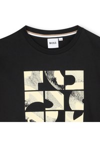 Fekete pamut póló, nagy grafikai mintával bézs és szürke árnyalatokban, klasszikus kerek nyakkivágással és a hátulján található címkével.