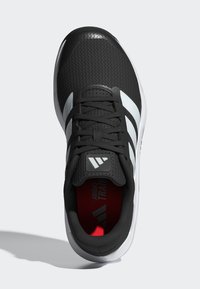 Baskets de sport noires avec tige en maille, accents blancs et semelle texturée. Comprend un orteil renforcé et une semelle intérieure rouge avec un logo.
