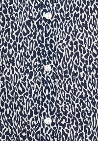 Leopardmønstret skjorte med et blått og hvitt mønster, knappelukking og teksturert stoff. Designet inkluderer uregelmessige flekker i varierende størrelser.