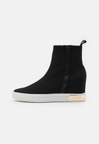 Černé pletené wedge tenisky s bílou podrážkou, které mají elegantní design, žebrovaný kotník a kovový detail na patě s logem "DKNY".