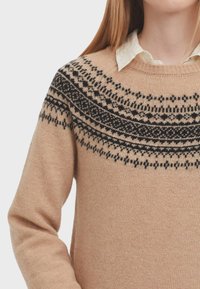 Beige Strickpullover mit einem schwarzen floralen Muster entlang des runden Ausschnitts. Weicher Stoff mit langen Ärmeln und gerippten Bündchen.