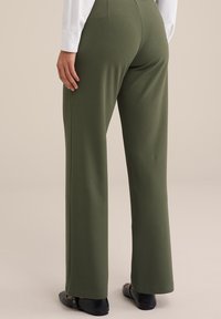 Pantaloni a gamba larga verde oliva realizzati in tessuto morbido, con una texture liscia e dettagli di cucitura discreti, abbinati a ballerine nere.