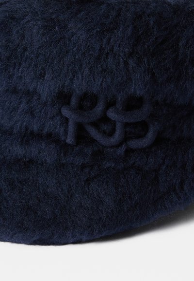 Jūrinės mėlynos dirbtinės vilnos skrybėlė, pasižyminti struktūrizuota forma ir tekstūruotu paviršiumi, su siuvinėtu "RS" logotipu atitinkančioje medžiagoje.