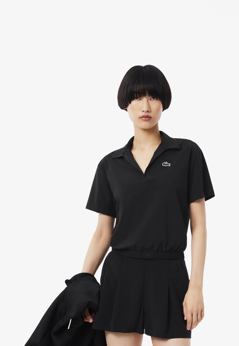 Polo negro de manga corta con cuello y cintura elástica, combinado con shorts negros. Presenta un logo verde en el pecho.