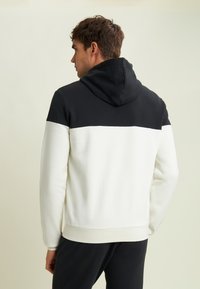 Felpa con cappuccio caratterizzata da una sezione superiore nera e una sezione inferiore bianca. Realizzata in tessuto morbido, presenta polsini e orlo a coste.