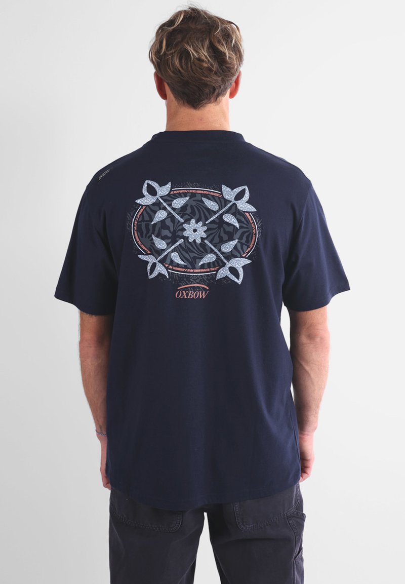 T-shirt bleu marine en coton avec un design graphique floral circulaire au dos, présentant des accents bleu clair et blanc.