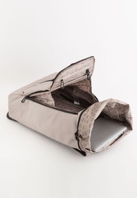 Geantă de laptop bej cu un exterior neted, fermoare deschise și un interior cu un model geometric. Conține un laptop argintiu.