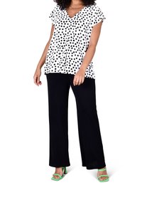 Vit blus med svarta prickar, V-ringning, korta ärmar; kombinerad med svarta vida byxor och gröna klacksandaler.