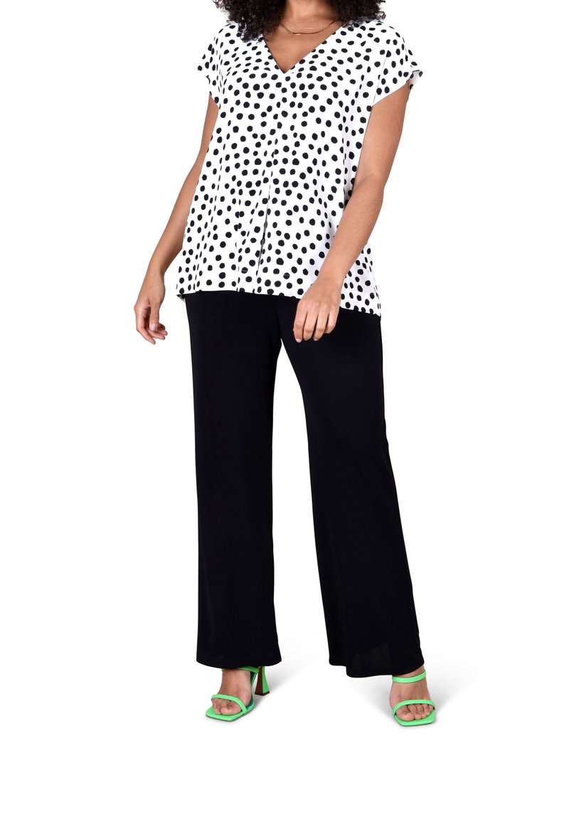 Vit blus med svarta prickar, V-ringning, korta ärmar; kombinerad med svarta vida byxor och gröna klacksandaler.