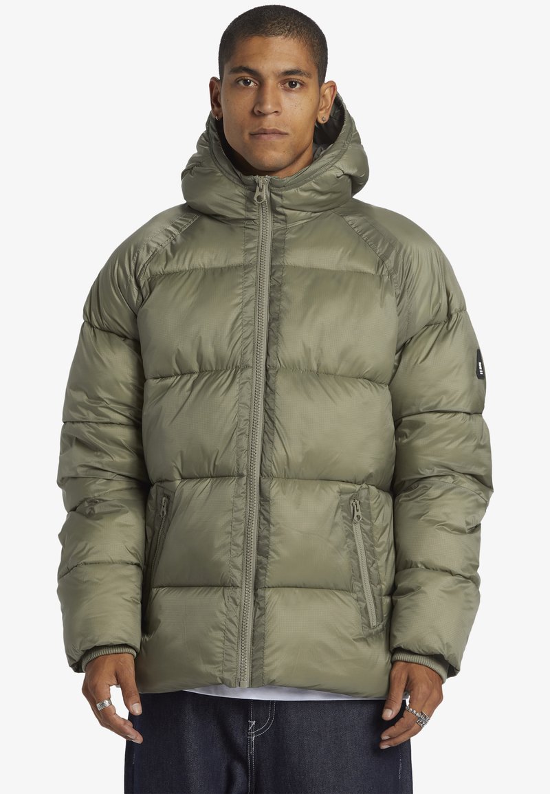 Olivgrön puffjacka med huva, framdragkedja och sidofickor. Har tjocka vadderingar och en slät, glänsande yta.