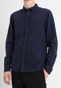 Navy blauwe shirt met lange mouwen, knoopsluiting en een subtiele patroonstructuur. Heeft een klassieke kraag en een getailleerd ontwerp.