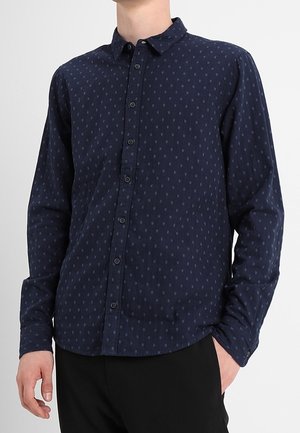 Chemise bleu marine à manches longues, fermeture à boutons et texture avec un motif subtil. Dotée d'un col classique et d'une coupe ajustée.