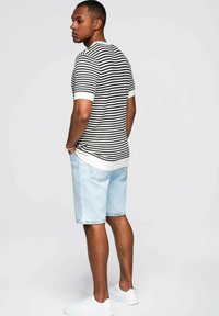 Camisa de punto a rayas en blanco y negro con mangas cortas, combinada con pantalones cortos de mezclilla azul claro y zapatillas blancas.