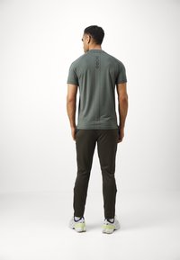 Grünes, kurzärmliges Sportshirt mit einem vertikalen schwarzen "BORG"-Logo auf dem Rücken. Kombiniert mit dunkelgrünen Hosen und Sportschuhen.