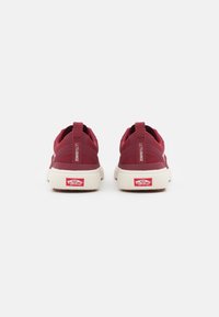 Scarpe slip-on in rete rossa con una soletta bianca, dettagli testurizzati e un patch con logo sul tallone. Presentano una linguetta per indossarle facilmente.