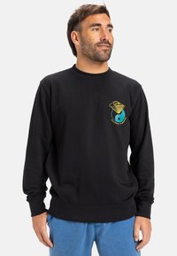 Black sweatshirt with long sleeves, crew neck, and elastic hem. Features a colorful graphic design on the left chest. Soft fabric texture.