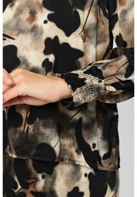 Långärmad blus med ett abstrakt mönster i svart, brunt och beige. Har detaljer med smockade manschetter och ett mjukt, lätt tyg.